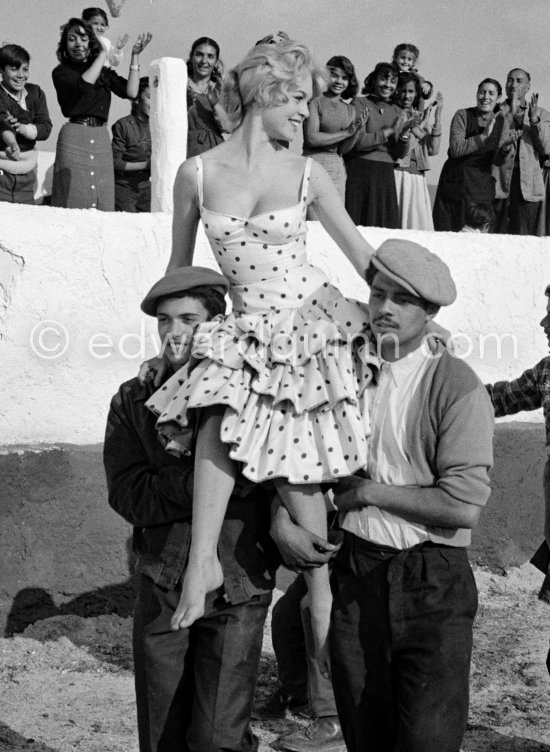 Brigitte Bardot during the filming of the last scenes of „Les Bijoutiers du clair de lune“ (“The Night Heaven Fell”), on the grounds of the Victorine Film Studios in Nice. Directing the film is Brigitte’s ex-husband Vadim. Brigitte is carried by two gipsies. The scene is supposed to represent Brigitte being carried victoriously out of the bull ring, after having given battle to a bull. All people in the back, young and old, are gipsies. Nice 1958. - Photo by Edward Quinn