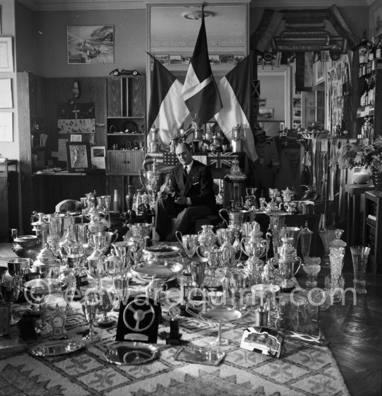 Louis Chiron at his museum of the victories: This photo on which are grouped the trophies of Chiron, summarizes thirty years of racing. One sees cups of Alfonso XIII., the Queen of England, the president of the Spanish Republic, Mussolini, the King of Italy, the Sultan of Morocco. The Count of Paris dedicated a photo "A Chiron the Centaur" to him. Monaco 1954. - Photo by Edward Quinn