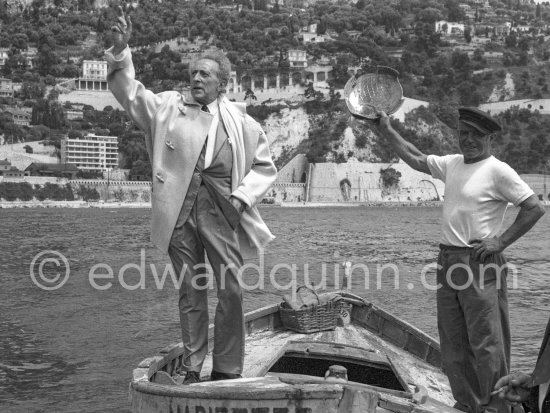 On the docks of the harbor at Villefranche-sur-Mer Jean Cocteau receives in a fishnet a life-size gold sardine from fisherman Paul Dunan (right), known as \'\'The Pirate\'\'. This present, created by a Nicois jeweller, is from the fishermen as a thank-you for the restoration and decoration works undertaken by the writer on the Chapelle Saint Pierre. Villefranche-Sur-Mer 1959. - Photo by Edward Quinn