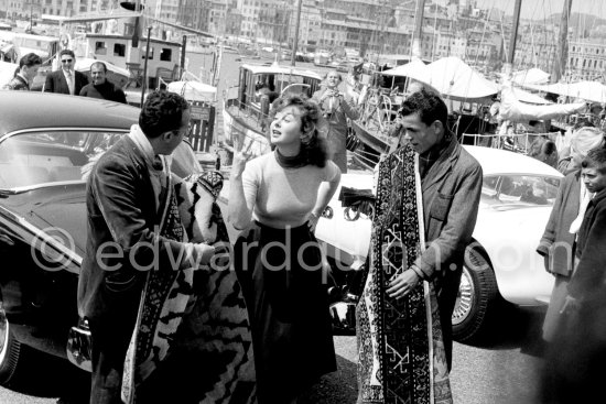 Foreign carpet sellers, trying to convince Susan Hayward to acquire one of these beautiful pieces. Cannes Film Festival 1956. Car: Studebaker - Photo by Edward Quinn