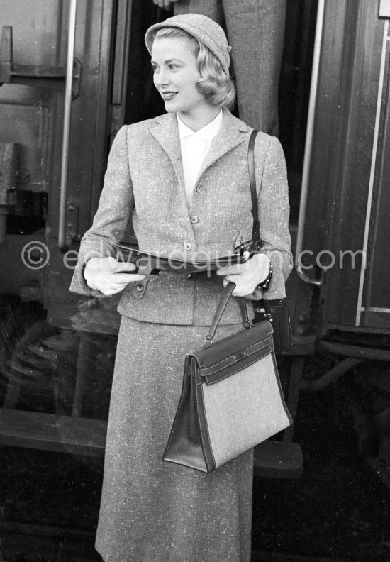 Grace Kelly with the original Kelly Bag and her Rolleiflex camera arriving at Cannes station 1955. - Photo by Edward Quinn