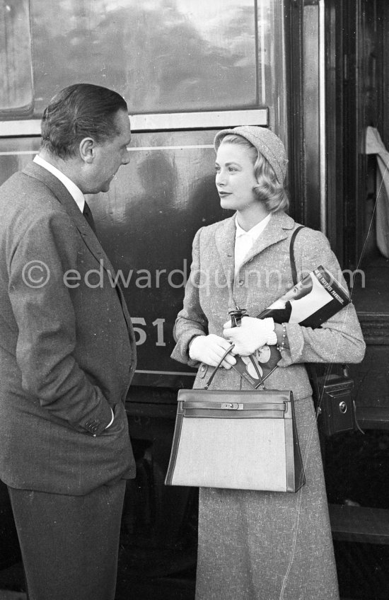 Grace Kelly with the original Kelly Bag and her Rolleiflex camera arriving at Cannes station 1955. On the left the Paramount representative in France. - Photo by Edward Quinn