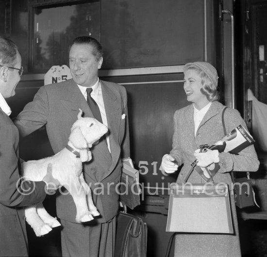 Grace Kelly with the original Kelly Bag and her Rolleiflex camera arriving at Cannes station 1955 is all smiles over the toy animal presented upon her arrival by the Paramount representative in France. - Photo by Edward Quinn