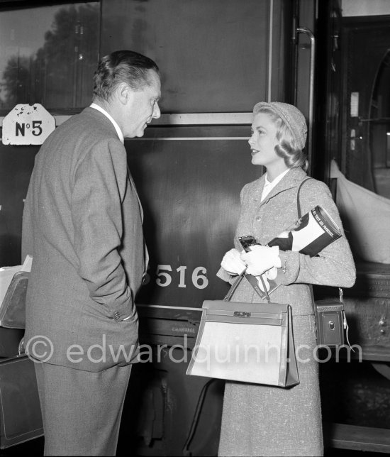 Grace Kelly with the original Kelly Bag and her Rolleiflex camera arriving at Cannes station 1955. On the left the Paramount representative in France. - Photo by Edward Quinn