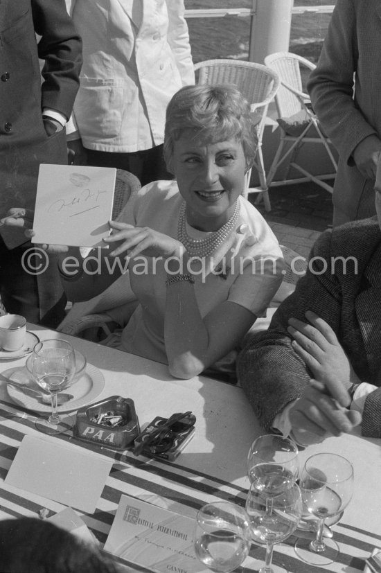 Michèle Morgan showing her autograph at lunch during the Cannes Film Festival 1956. Place card of François Mitterand in the foreground. - Photo by Edward Quinn