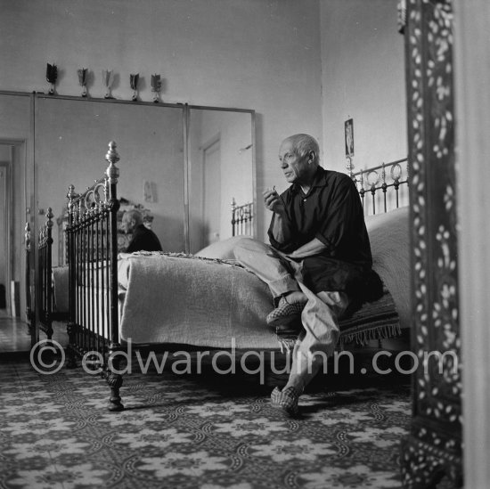 Pablo Picasso pensively, with baggy, unpressed trousers, a very loose-fitting shirt and carpet slippers, in his bedroom at La Galloise, Vallauris 1954. - Photo by Edward Quinn