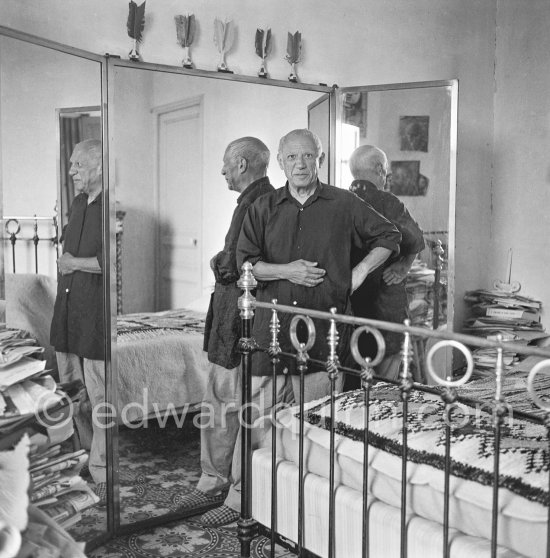 Pablo Picasso completely at ease, with baggy, unpressed trousers, a very loose-fitting shirt and carpet slippers, in his bedroom with three mirrors at La Galloise, Vallauris 1954. - Photo by Edward Quinn