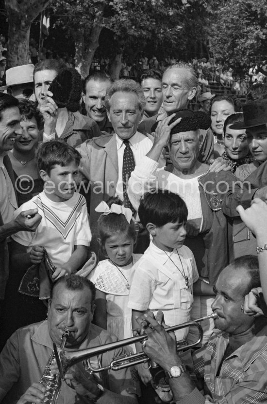 At Pablo Picasso\'s arrival on the village square where the corrida is to be held the band blares out some of his favourite Spanish melodies. From left: Javier Vilató, his wife Germaine Lascaux, Jean Cocteau, Jacques-Henri Lartigue, photographer (behind Cocteau), his wife Florette, Pablo Picasso, Jacqueline, Maya Picasso, Paloma Picasso and Claude Picasso. Vallauris 1955. - Photo by Edward Quinn
