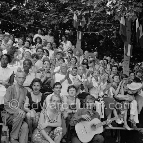 Pablo Picasso on the grandstand at the corrida surrounded by his family and friends. Lartigue and his wife Florette, Vilató and wife Germaine Lascaux, Jacqueline, Maya Picasso, Jean Cocteau, Francine Weisweiller, Dr. Jeanne Creff (acupuncturist of Pablo Picasso), with the guitar the son of the writer José Herrera-Petere. Vallauris 1955. - Photo by Edward Quinn