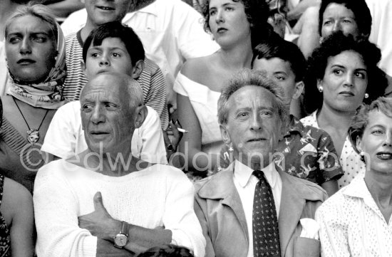 On the grandstand of a bullfight put on in Pablo Picasso\'s honor. From left: Pablo Picasso, Jean Cocteau. Behind them Maya Picasso with a pendent by Pablo Picasso, Claude Picasso, Gérard and Inès Sassier. Vallauris 1955. - Photo by Edward Quinn