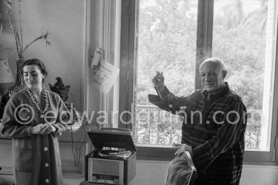 Listening to music from a 45 rpm single on a turntable. Pablo Picasso and Jacqueline on his 75th birthday 25 Oct. Note on the paper on the wall: Penrose arrive par le train à 10h lundi. La Californie, Cannes 1956. - Photo by Edward Quinn