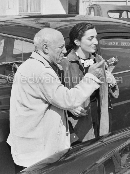 Pablo Picasso with Jacqueline in Cannes on Mayday. Jacqueline is holding some sprigs of "muguet", the traditional flower of the day. She\'s wearing a ceramic necklace made for her by Pablo Picasso. La Croisette, Cannes 1957. - Photo by Edward Quinn