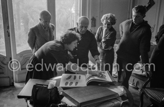 Pablo Picasso looks at the copy of a deluxe edition of a book of poems by Pierre Reverdy, for which he has made the illustrations. Gathered around him as he comments on the book are Madame Weill, a Paris publisher, the writer Michel Leiris, his wife Louise Leiris, owner with Daniel-Henry Kahnweiler of the Leiris Gallery Paris, André Weill, publisher of some deluxe editions of Pablo Picasso\'s work and Paulo Picasso. La Californie, Cannes 1959. - Photo by Edward Quinn
