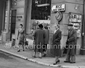 Two ladies viewing some potteries in a shop window and a couple going to cross the road, oblivious that a famous actress, Ingrid Bergman is walking just beside them. (She came with her three children for a short trip to Monaco, on her way to Spain). Monte Carlo 1954. - Photo by Edward Quinn