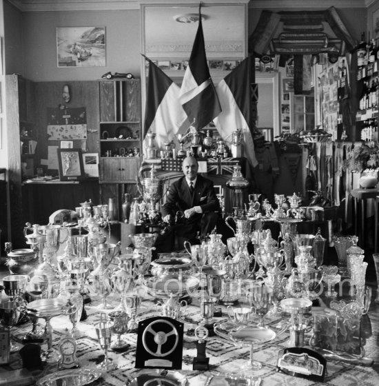 Louis Chiron at his museum of the victories: This photo on which are grouped the trophies of Chiron, summarizes thirty years of racing. One sees cups of Alfonso XIII., the Queen of England, the president of the Spanish Republic, Mussolini, the King of Italy, the Sultan of Morocco. The Count of Paris dedicated a photo "A Chiron the Centaur" to him. Monaco 1954. - Photo by Edward Quinn