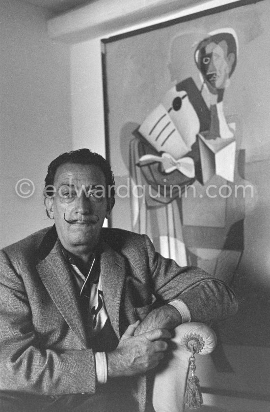 Salvador Dalí sits in front of his painting "Taula davant el mar (Table in front of the Sea) Homage to Eric Satie". Portlligat, Cadaqués 1957. - Photo by Edward Quinn