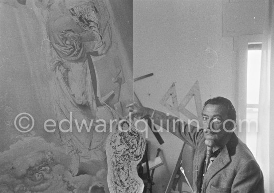 Salvador Dalí poses at his studio with his ink drawing of a madonna and her child and the painting "Cosmic Madonna", finished in 1958. At Salvador Dalí's house, Portlligat, Cadaqués, 1957. - Photo by Edward Quinn