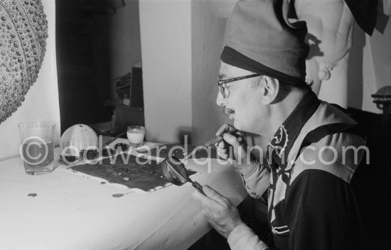 Salvador Dalí demonstrates the origin of the "oursin", a liquid which takes on a particular form. Here he is seen using milk and water. The display board shows a sea urchin fossile. At Salvador Dalí\'s house, Portlligat, Cadaqués 1957. - Photo by Edward Quinn