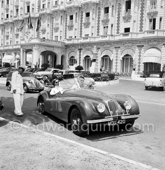 Clark Gable and "fiancée" Suzanne Dadolle, French model, in front of Carlton Hotel. Cannes 1953. Car: 1951 Jaguar XK120 OTS Battleship grey/red, Car today see https://bit.ly/3kLirWW - Photo by Edward Quinn