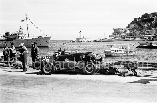 The cars of Mike Hawthorn, (28) Ferrari-Lancia D50 and Peter Collins, (26) Ferrari 801 in the barriers while Juan Manuel Fangio, (32) Maserati 250F passes. Yacht Trenora in the background. The incident happend in lap 4 of the 1957 Monaco Grand Prix after leader Stirling Moss "lost" his Vanwall in the chicane. Peter Collins swerved to avoid Moss but hit the wall while Mike Hawthorn rammed Tony Brooks who braked hard to avoid the cars in front of him. - Photo by Edward Quinn