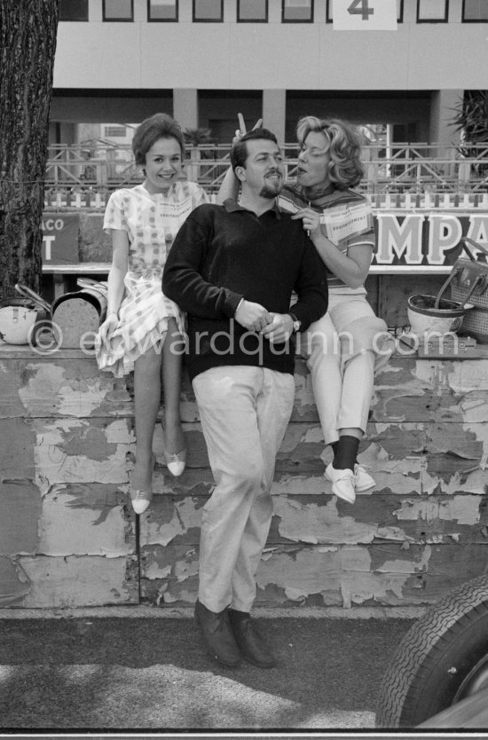 Gags in the pit, as Joakim Bonnier, the Swedish driver, poses for a picture, Monique Schell, Harry Schell\'s wife, makes a hidden v-sign. On the left is another racing fan, pretty Carine Kollen. Monaco Grand Prix 1959. - Photo by Edward Quinn