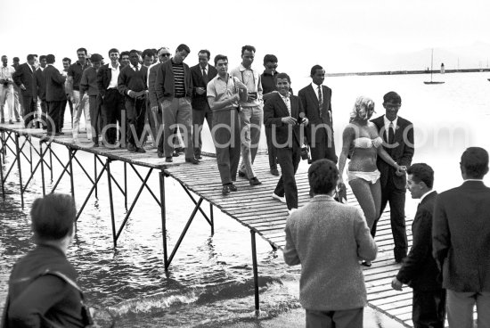 After a photo session at the beach of Cannes, a pretty winner of a "Miss" contest leads the crowd to safer grounds. Cannes Film Festival 1960. - Photo by Edward Quinn