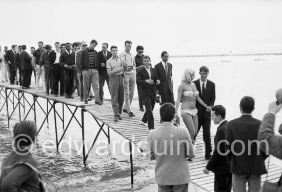 After a photo session at the beach of Cannes, a pretty winner of a "Miss" contest leads the crowd to safer grounds. Cannes Film Festival 1960. - Photo by Edward Quinn