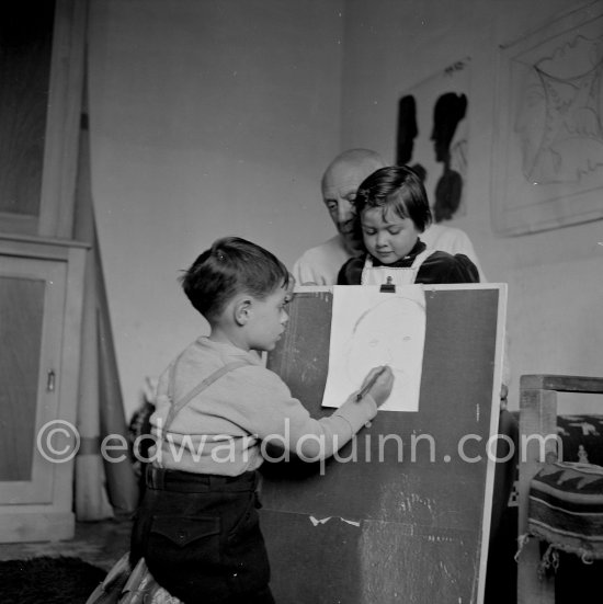 Encouraged by his father, Claude Picasso tries to do a portrait of Pablo Picasso, portraying him with a round face, deep furrows on his forehead, a triangle for a nose, and streaks of hair on the sides of his head. La Galloise, Vallauris 16.4.1953. - Photo by Edward Quinn