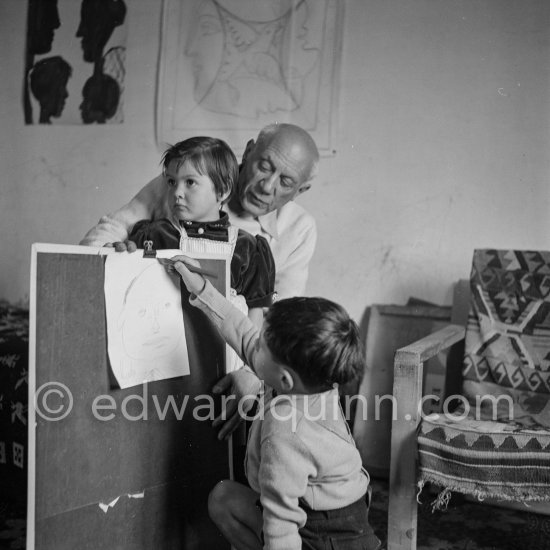Encouraged by his father, Claude Picasso tries to do a portrait of Pablo Picasso, portraying him with a round face, deep furrows on his forehead, a triangle for a nose, and streaks of hair on the sides of his head. La Galloise, Vallauris 16.4.1953. - Photo by Edward Quinn