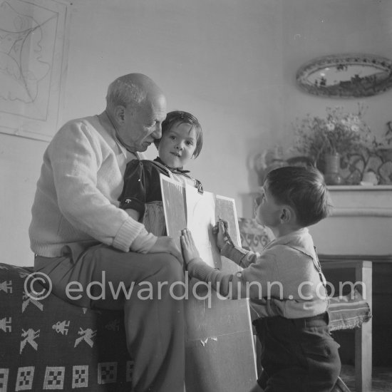 Encouraged by his father, Claude Picasso tries to do a portrait of Pablo Picasso, portraying him with a round face, deep furrows on his forehead, a triangle for a nose, and streaks of hair on the sides of his head. La Galloise, Vallauris 16.4.1953. - Photo by Edward Quinn