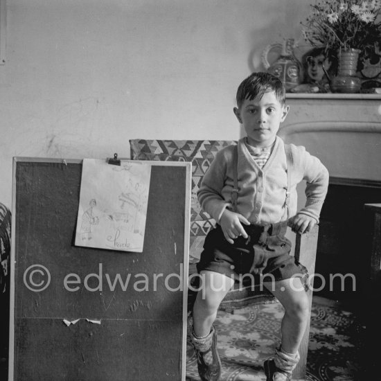 Encouraged by his father, Claude Picasso tries to do a portrait of Pablo Picasso, portraying him with a round face, deep furrows on his forehead, a triangle for a nose, and streaks of hair on the sides of his head. La Galloise, Vallauris 16.4.1953. - Photo by Edward Quinn