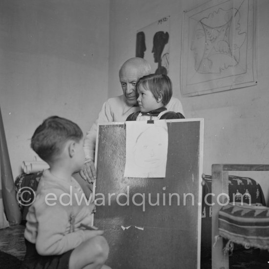 Encouraged by his father, Claude Picasso tries to do a portrait of Pablo Picasso, portraying him with a round face, deep furrows on his forehead, a triangle for a nose, and streaks of hair on the sides of his head. La Galloise, Vallauris 16.4.1953. - Photo by Edward Quinn