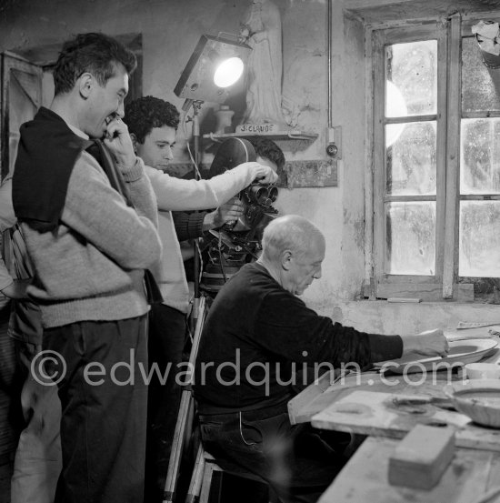 Pablo Picasso using a sharp instrument to scrape the surface of a clay plate as he designs a portrait. During filming of "Pablo Picasso", director Luciano Emmer, (left) and Pablo Picasso. Madoura pottery, Vallauris 14.10.1953. - Photo by Edward Quinn