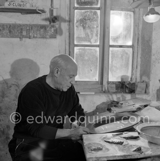 Pablo Picasso using a sharp instrument to scrape the surface of a clay plate as he designs a portrait. During filming of "Pablo Picasso", director Luciano Emmer, (left) and Pablo Picasso. Madoura pottery, Vallauris 14.10.1953. - Photo by Edward Quinn