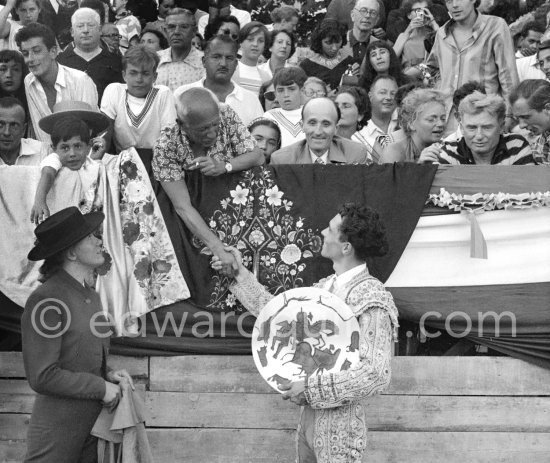 Local Corrida at Vallauris. Pablo Picasso having given a ceramic plate as a price, congratulates Pepe Luis Marca. On the left is French lady bullfighter Pierrette Le Bourdiec. On the grandstand from left Michel Leiris, Claude Picasso, beside Pablo Picasso Paul Derigon, the mayor of Vallauris, Hélène Parmelin, Edouard Pignon. Vallauris 1954. - Photo by Edward Quinn