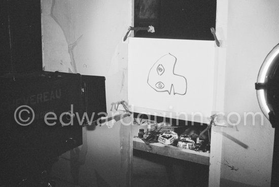 During filming of "Le mystère Picasso". Pablo Picasso working on "Tête de femme" with colored ink. He had a frame constructed on which he could stretch a transluscent piece of paper. He drew on one side, and the camera filmed the drawing being born from the other side. Nice, Studios de la Victorine 1955. - Photo by Edward Quinn