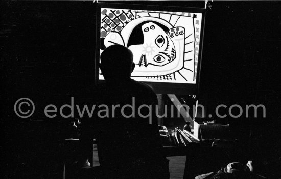 During filming of "Le mystère Picasso". Pablo Picasso working on "Tête de femme" with colored ink. He had a frame constructed on which he could stretch a transluscent piece of paper. He drew on one side, and the camera filmed the drawing being born from the other side. Nice, Studios de la Victorine 1955. - Photo by Edward Quinn