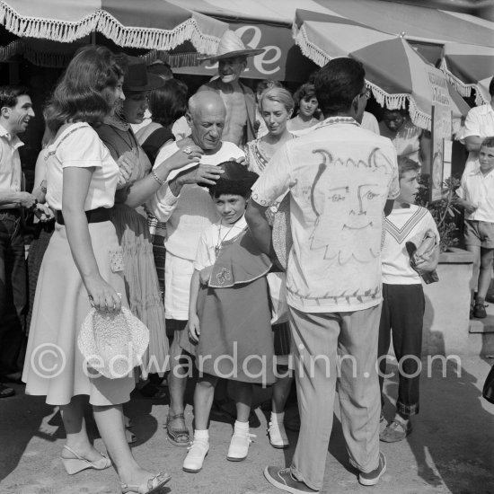 From left Javier Vilató, unknown girl, Maya Picasso, Pablo Picasso, Claude Picasso, photographer Jacques-Henri Lartigue with hat in the background and a tourist wearing a shirt with a Pablo Picasso drawing. In front of restaurant Le Vallauris. Vallauris 1955. - Photo by Edward Quinn