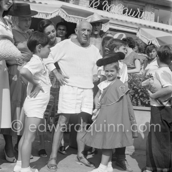 Pablo Picasso proudly poses with daughter Maya Picasso (left), son Claude Picasso and Paloma Picasso in miniature toreador costumes. Photographer Jacques-Henri Lartigue in the background with hat, his wife Florette. In front of restaurant Le Vallauris. Vallauris 1955. - Photo by Edward Quinn