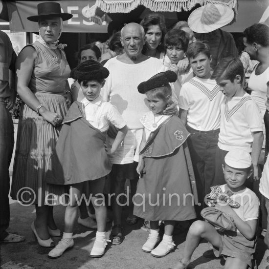 Pablo Picasso proudly poses with daughter Maya Picasso (left), son Claude Picasso and Paloma Picasso in miniature toreador costumes. Photographer Jacques-Henri Lartigue in the background with hat. In front of restaurant Le Vallauris. Vallauris 1955. - Photo by Edward Quinn