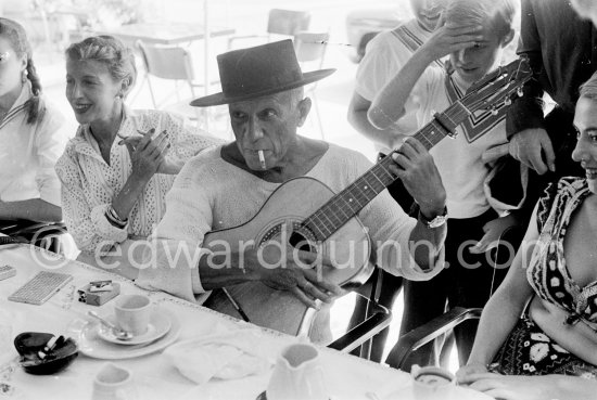 In Spanish mood Pablo Picasso wears a "chapeau cordouan" as he pretends to play guitar at restaurant Le Vallauris. Vallauris 11.8.1955. - Photo by Edward Quinn