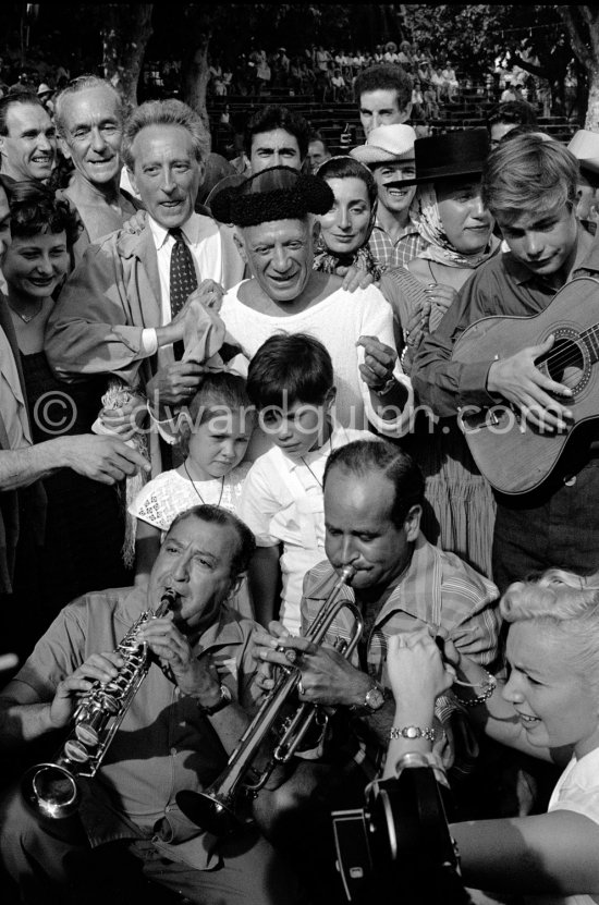 At Pablo Picasso\'s arrival on the village square where the corrida is to be held, the band blares out some of his favourite Spanish melodies. From left: Javier Vilató\'s wife Germaine Lascaux, Jacques-Henri Lartigue, his wife Florette, Jean Cocteau, Pablo Picasso, Jacqueline, Maya Picasso and in front of Pablo Picasso Paloma Picasso and Claude Picasso, with the guitar the son of the writer José Herrera-Petere. Vallauris 1955. - Photo by Edward Quinn