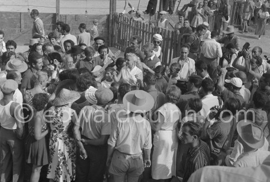 At Pablo Picasso's arrival on the village square where the corrida is to be held the band blares out some of his favourite Spanish melodies. Pablo Picasso in the crowd surrounded by his family and friends. Vallauris 1955. - Photo by Edward Quinn