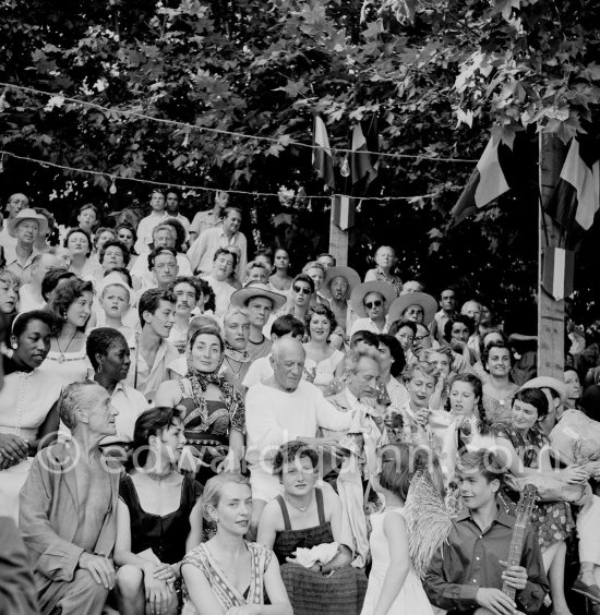 Pablo Picasso on the grandstand at the corrida surrounded by his family and friends. Lartigue and wife Florette, Vilató and wife Germaine Lascaux, Jacqueline, Maya Picasso, Jean Cocteau, Francine Weisweiller and her daughter Carole, Dr. Jeanne Creff (acupuncturist of Pablo Picasso), with the guitar the son of the writer José Herrera-Petere. Vallauris 1955. - Photo by Edward Quinn