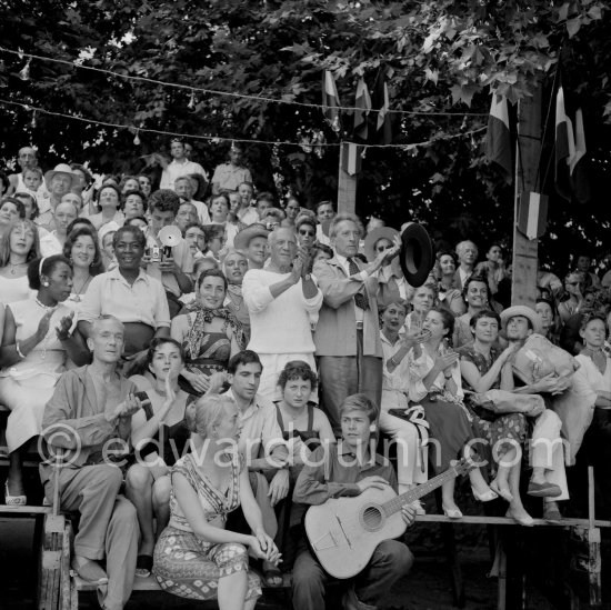 Pablo Picasso on the grandstand at the corrida surrounded by his family and friends. Lartigue and his wife Florette, Vilató and wife Germaine Lascaux, Jacqueline, Maya Picasso, Jean Cocteau, Francine Weisweiller and her daughter Carole, Dr. Jeanne Creff (acupuncturist of Pablo Picasso), with the guitar the son of the writer José Herrera-Petere. Vallauris 1955. - Photo by Edward Quinn