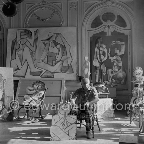 Pablo Picasso holding a cutout figure of a faun, with another faun "seated" on the rocking-chair. Behind Pablo Picasso, two paintings done in 1956. La Californie, Cannes 1956. - Photo by Edward Quinn