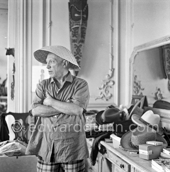 To strike a pose, Pablo Picasso tries on hats from his collection for his own amusement and that of his guests. La Californie, Cannes 1956. - Photo by Edward Quinn