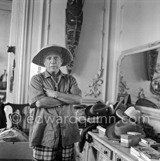 To strike a pose, Pablo Picasso tries on hats from his collection for his own amusement and that of his guests. La Californie, Cannes 1956. - Photo by Edward Quinn