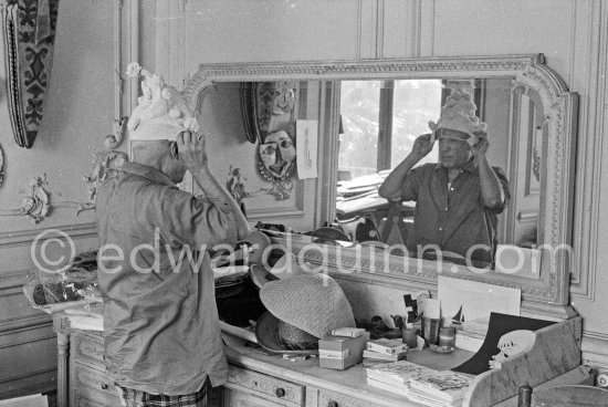 To strike a pose, Pablo Picasso tries on hats from his collection for his own amusement and that of his guests. La Californie, Cannes 1956. - Photo by Edward Quinn