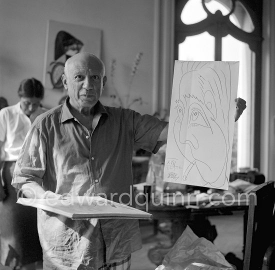 Pablo Picasso shows a drawing he has done of his friend, the writer Prévert. Swiss collector Anna Blankart in the background. La Californie, Cannes 24.10.1956. (Eve of Pablo Picasso\'s 75th birthday). - Photo by Edward Quinn